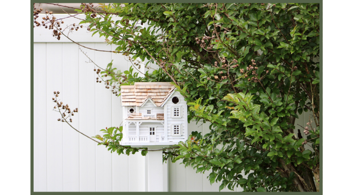 white bird house in a tree in front of a fence