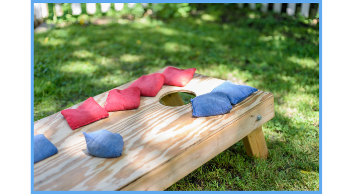 cornhole on a green lawn with eight bean bags on top of its wood
