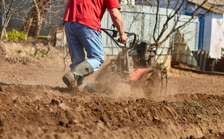a man pushes a rototiller along a yard full of dirt before laying down sod