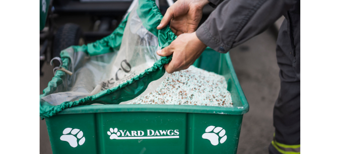 lawn care technician pulls cover over fertilizer spreader filled with granules of fertilizer