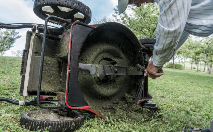 man cleans mower deck of grass