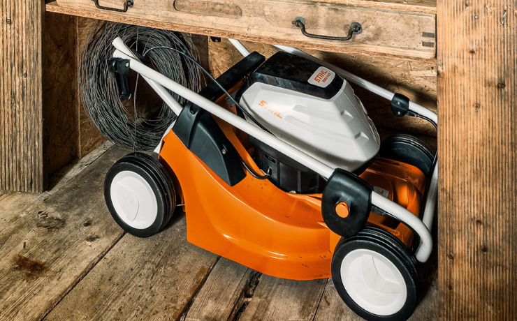 lawn mower stored under a shelf in storage 