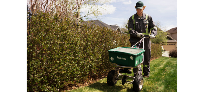 lawn care technician uses a spreader to apply fertilizer to a lawn
